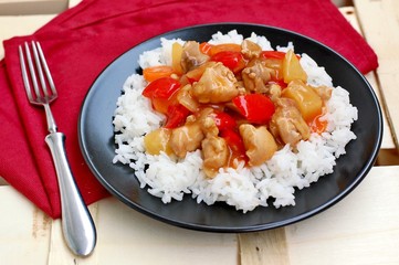 Sweet and sour food with rice,red pepper,pineapple,onion and chicken meat on red cloth on black plate on wooden background