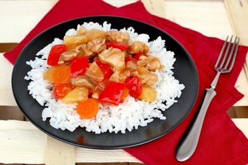 Sweet and sour food with rice,red pepper,pineapple,onion and chicken meat on red cloth on black plate on wooden background