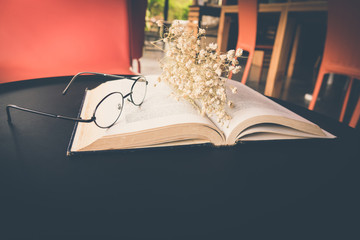 Old book open on table with reading glasses and classic flower