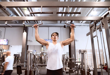 Hispanic man in gym doing pull-ups on horizontal bar