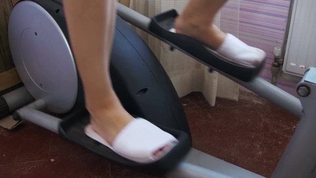 Young Woman Exercising on Elliptical Machine at Home. Sport woman is engaged in sports at home. Girl on the Elliptical Trainer. Home fitness