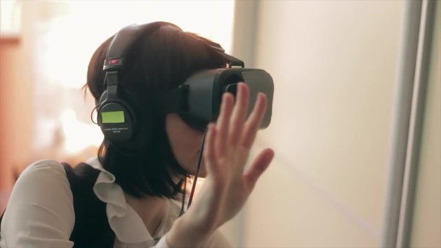 Young brunette woman playing game using VR-helmet for smart phones. Augmented reality device allows to deep into virtual space