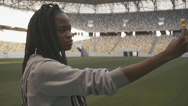 The portrait of the young afro-american girl with the dark brown hair taking selfie in the sport stadium