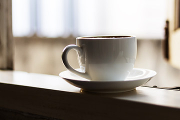 Hot coffee in a white cup is at the window.