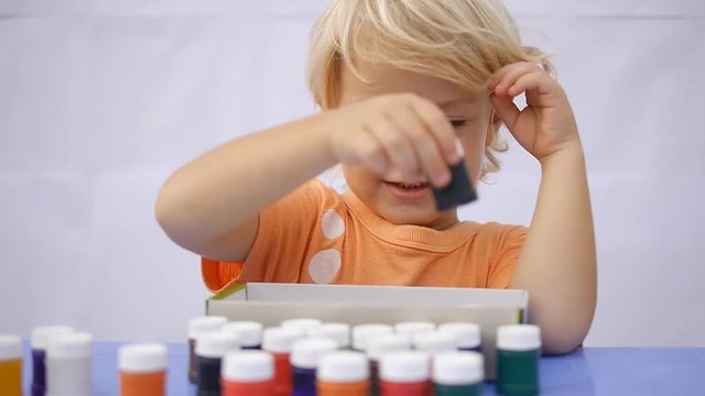 Cute little child taking out of the box colorful paint. Showing empty box and smiling on white wall background 50fps"