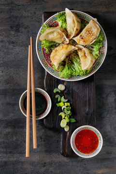 Gyozas potstickers on lettuce salad with sauces. Served in traditional china plate with chopsticks and spring onion on wood serving board over old metal background. Top view, space. Asian dinner