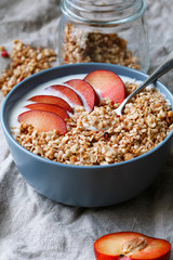 Close-up on a blue bowl with breakfast with oat flakes, yogurt and pieces of red plum on table. Copy space.