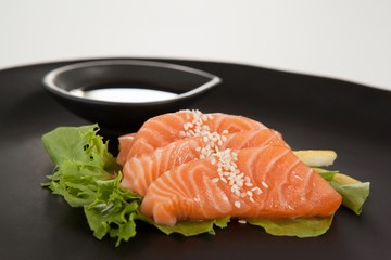 Four sashimi sushi served with soy sauce in black plate