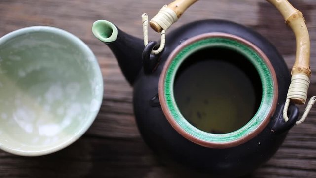 Brewing tea in a little Asian teapot and pouring it into a cup.