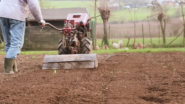 Farmer plowing the field with rototiller. 