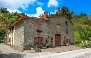 Fototapeta na wymiar Traditional italian stone house near the road.Flowers on the windows and wooden shutters.Italy