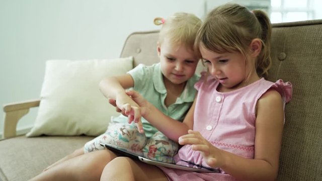 Two little sisters fun playing digital tablet indoor