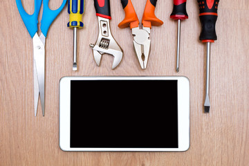 Construction tools and a tablet on a wood background. Scissors, ruler, pliers, screwdriver
