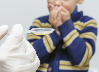 Doctor in white gloves hand giving spoon dose of medicine drinking syrup. Little boy refusing to...