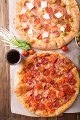 Rustic pizza with salami, mozzarellabasil top view with copy space. Two pizzas on a wooden table. Pizza salami on wooden background. Pizza salami with tomatoes and olives.