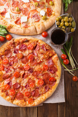 Rustic pizza with salami, mozzarellabasil top view with copy space. Two pizzas on a wooden table. Pizza salami on wooden background. Pizza salami with tomatoes and olives.