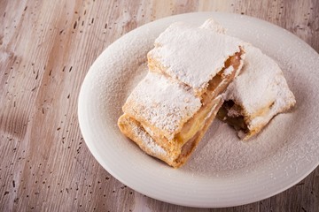Two slices of apple strudel with powder sugar on white saucer