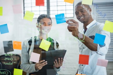 Business colleagues discussing over sticky notes on glass