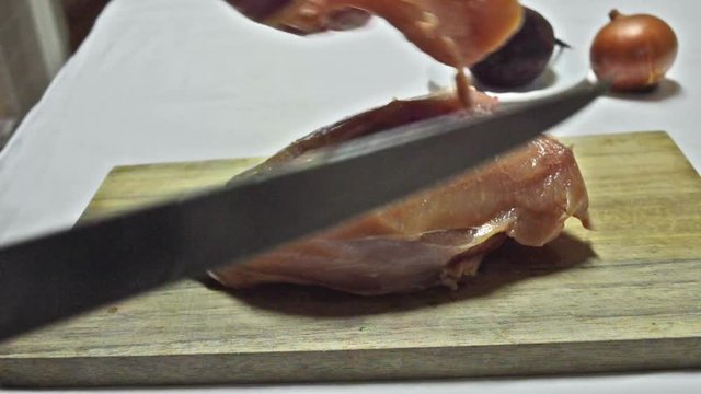 Female hands sliced chicken breast on a wooden board into pieces close-up