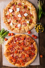 Rustic pizza with salami, mozzarellabasil top view with copy space. Two pizzas on a wooden table. Pizza salami on wooden background. Pizza salami with tomatoes and olives