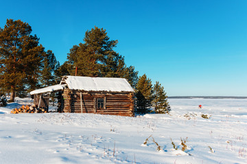 An old fishing hut in the snow. Away people on the ice.