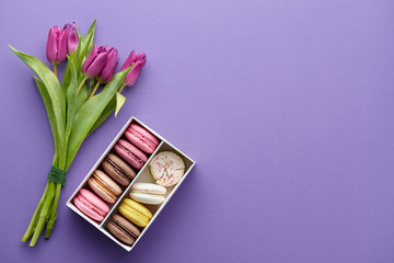 Spring purple tulips and box of colorful macarons on purple background, top view
