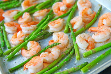 Fresh asparagus with shrimp on a baking sheet with coarse salt, olive oil and black pepper