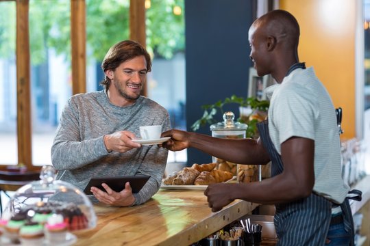 Waiter serving coffee to male customer