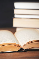 Close-up of an open book next to several stacked books. Vertical shoot.