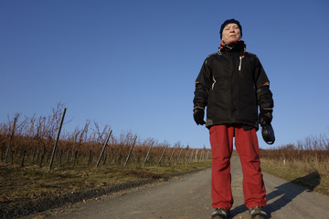 eine ältere frau geht auf einem feldweg im weinberg