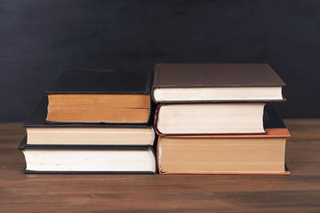 Books stacked on brown wooden table and black background.