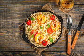 Seafood. Shellfish. Pasta with grilled prawns shrimps, with tomatoes, fresh herbs (basil) and spices. On  cast-iron frying pan, wooden rustic table, with glass of white wine, Copy space top view