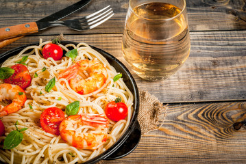 Seafood. Shellfish. Pasta with grilled prawns shrimps, with tomatoes, fresh herbs (basil) and spices. On  cast-iron frying pan, wooden rustic table, with glass of white wine, Copy space