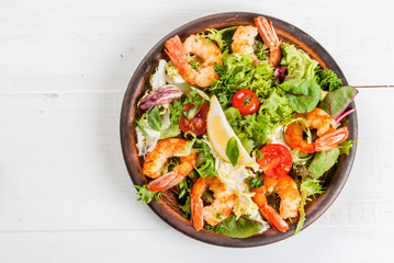 Seafood. Shellfish. Fresh lettuce salad with tomatoes, herbs and grilled fried shrimps prawns, on white table, top view, copy space