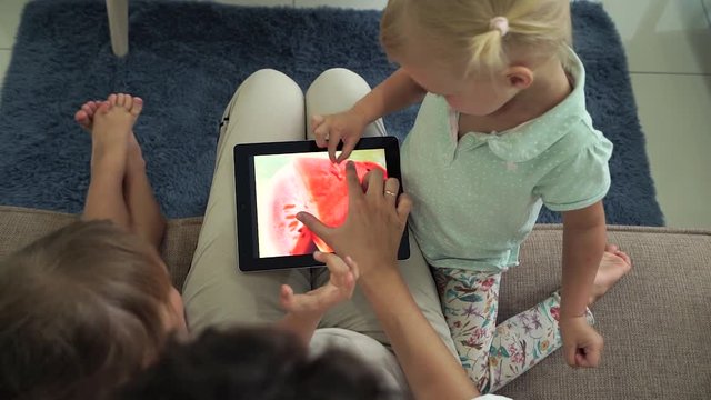 Mother with her daughters using digital tablet and see photos of exotic fruits