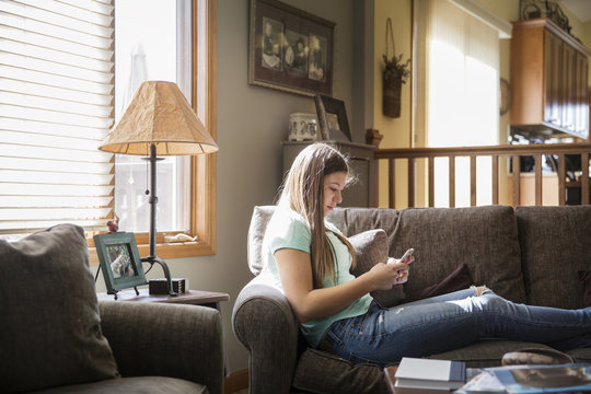 Teenage girl (16-17) sitting on sofa and using cell phone