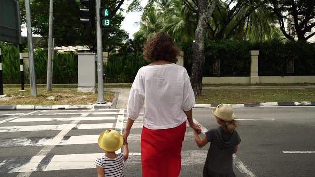 Young mother and her two daughters cross road at pedestrian crossing