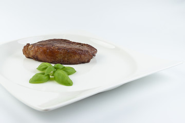Slice of barbecued cow beef (picanha) and basil leaves on a white dish with white background