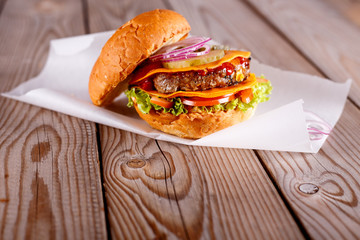 Outdoor big hamburger with beef, cheese, tomatoes and fried bacon on a wooden table