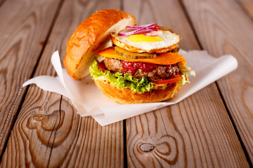 Big hamburger with beef, cheese and egg, tomatoes and fried bacon on a wooden table