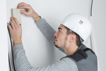 Man fitting thermostat controller to wall