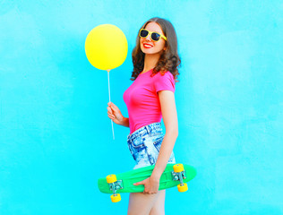 Fashion pretty woman with yellow air balloon and skateboard having fun over colorful blue background
