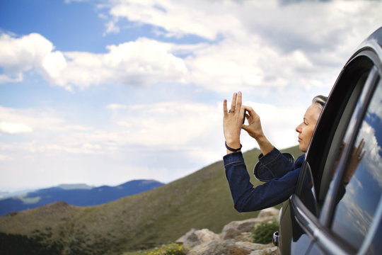 Woman taking picture of mountains out of car window