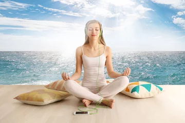  Young woman meditating in lotus pose on seascape background. Concept of music for sleep © Africa Studio
