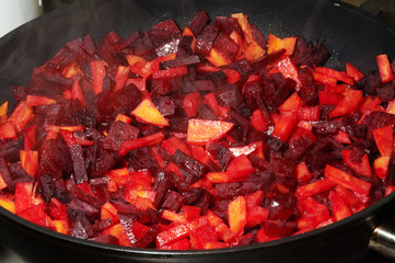 Cut-up red beet and carrot are frying in pan