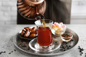 Pouring Turkish tea into traditional glass and sweets on metal tray closeup