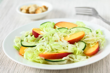 Fresh nectarine, cucumber and iceberg lettuce salad on plate, photographed with natural light (Selective Focus, Focus in the middle of the salad)