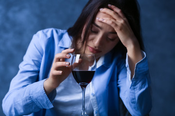 Depressed young woman drinking wine on grey wall background