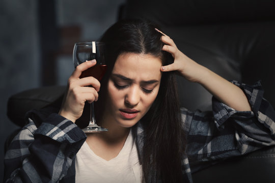 Depressed young woman drinking wine indoors