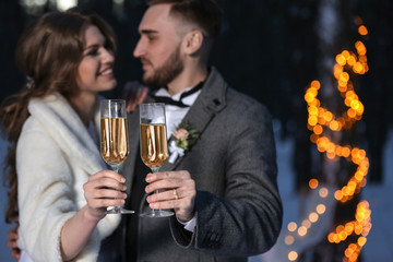 Happy wedding couple with glasses of champagne on winter evening